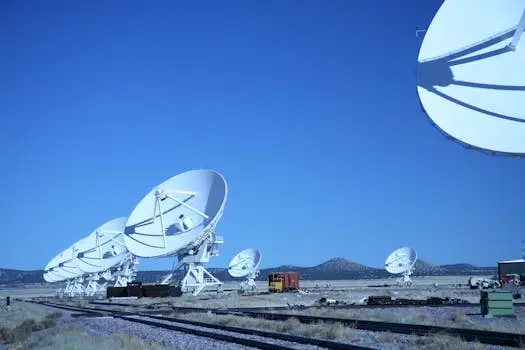 Multiple satellite dishes aligned in a field against a vibrant blue sky, showcasing modern communication technology.